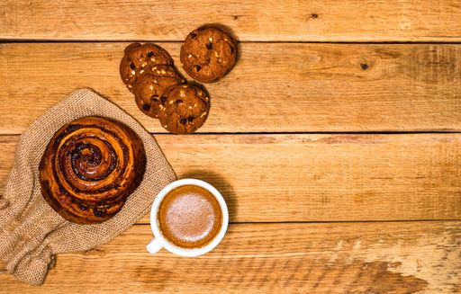 A top view of a croissant, biscuits and a cup of coffee on a wooden board