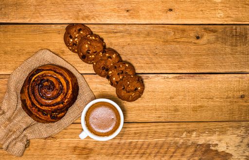 A top view of a fresh cinnamon roll and biscuit with coffee on a wooden table