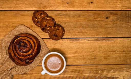 A top view of a fresh cinnamon roll and biscuit with coffee on a wooden table