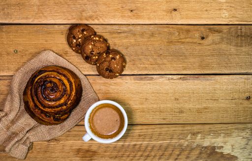 A top view of a croissant, biscuits and a cup of coffee on a wooden board