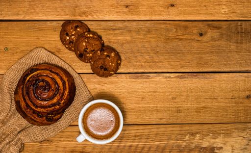 A top view of fresh puff pastries, desserts, and a coffee cup in the wooden background with a copy space
