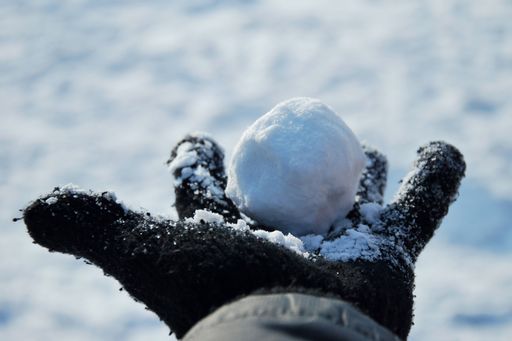 A closeup shot of a hand with a black glove holding a snowball
