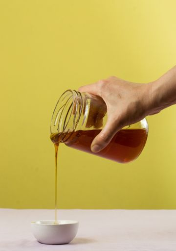 A hand pouring honey from a jar over a white bowl