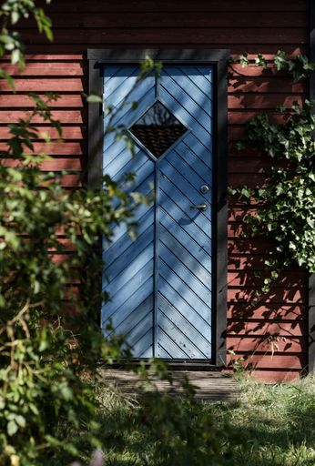 A closeup vertical shot of a blue wooden door of a small red barn in a forest