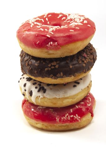 A vertical closeup of glazed doughnuts on each other on the table under the lights