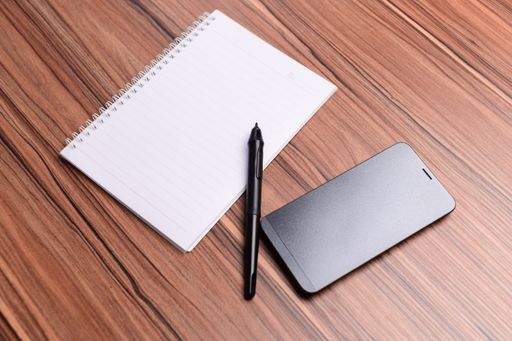 A shot of a notebook with black pen and smartphone on the wooden desk