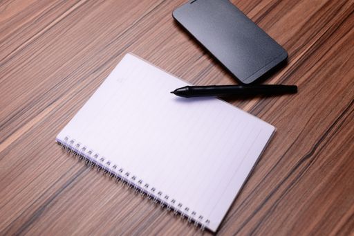A top view of a notebook and pen with a smartphone on the desk