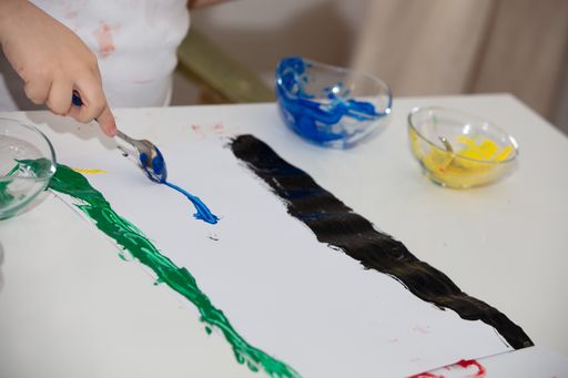 A high angle shot of a child painting with his hands and different colors of paint on a white page