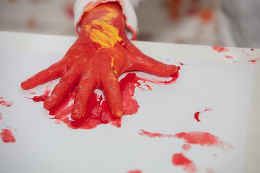 A high angle shot of a child painting with his hands and different colors of paint on a white page