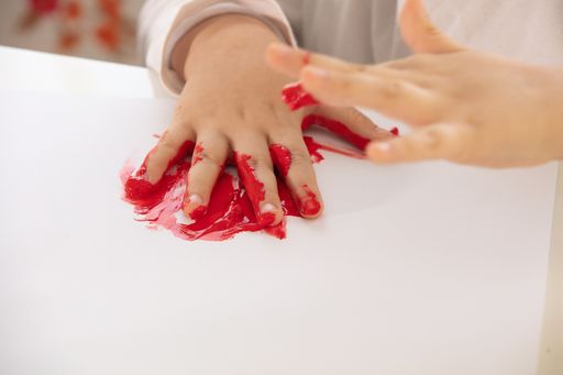 A high angle shot of a child painting with his hands and different colors of paint on a white page