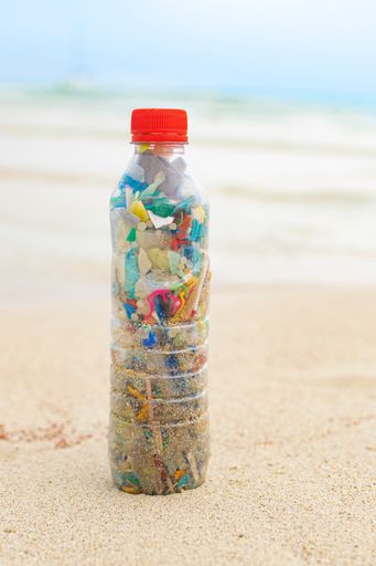 A vertical shot of a bottle filled with microplastics collected from the sea on the sand beach