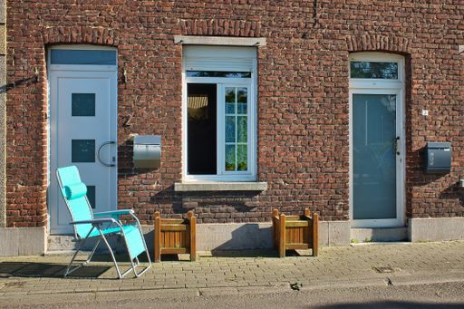 A shot of a blue chair in front of a brick house at daytime