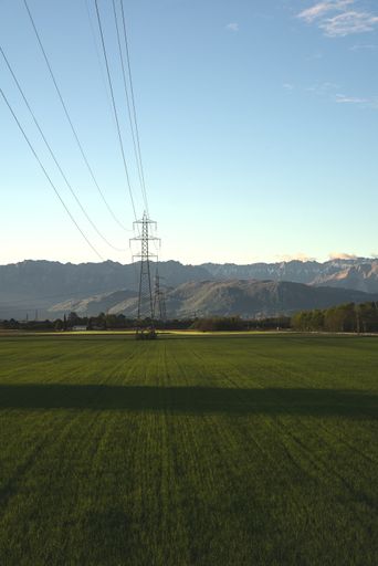 A vertical view of a green field with transmission tower during daylight