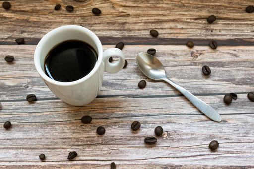 A high angle shot of a cup of coffee and a spoon on a wooden surface with scattered coffee beans