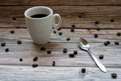 A high angle shot of a cup of coffee and a spoon on a wooden surface with scattered coffee beans