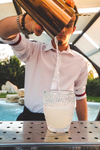 A professional Italian barman pouring cocktail into a glass from the shaker