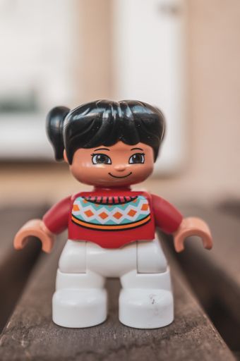 Plastic Lego Duplo girl figurine standing on a wooden surface in soft focus background.