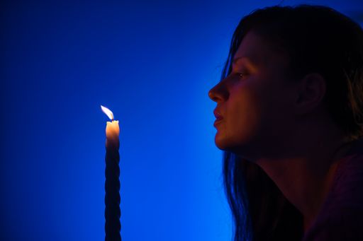 A Caucasian lady blowing a single candle isolated on a blue background