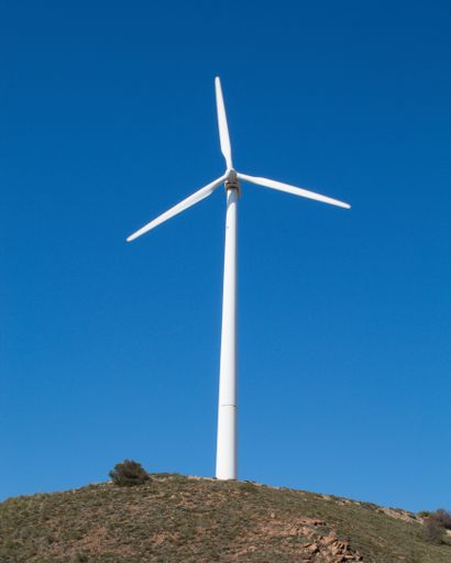 A vertical shot of a wind turbine with the clear skies in the background