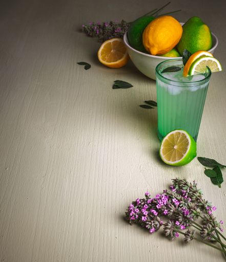 Refreshing lime and lemon drink with ice, garnished with mint and flowers, on a textured wooden table.