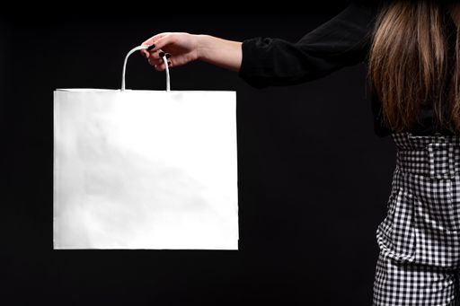 A closeup shot of a female hand holding a white shopping bag on black background