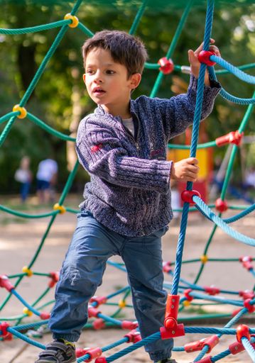 A young Polish Caucasian boy climbing on ropes at a playground in a park
