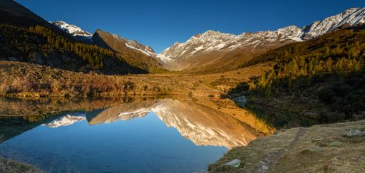 Reflection of autumn larch tree forest and mountain landscape in lake grundsee in wallis loetschental switzerland.