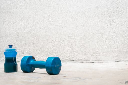 A used blue dumbbell and bottle o water on the floor on a white background