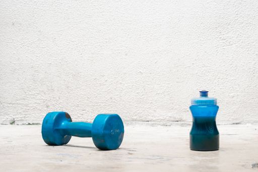 A used blue dumbbell and bottle of water on the floor on a white background