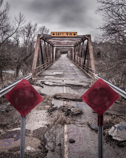A vertical shot of a broken old road on a bridge with closed red signs