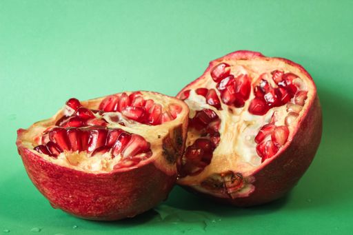 Close-up of a halved pomegranate on a green background. Juicy red seeds with natural shine, droplets adding freshness