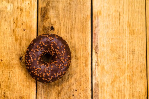 A top view of chocolate glazed donut with sprinkles on wooden board with copy space