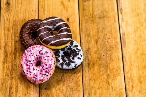 The colorful donuts on wooden table. Sweet icing sugar food with glazed sprinkles, a doughnut with chocolate frosting. Top view with copy space