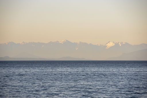 A wide landscape shot of a sea surrounded by mountains in the distance under a pink sky