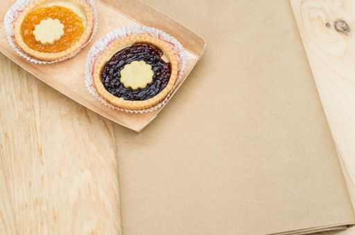 isolated apricot and cherry jam tart in a paper backing cup on a wood tabletop background with text space