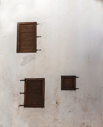 Three windows with wooden shutters of a house with white exterior walls