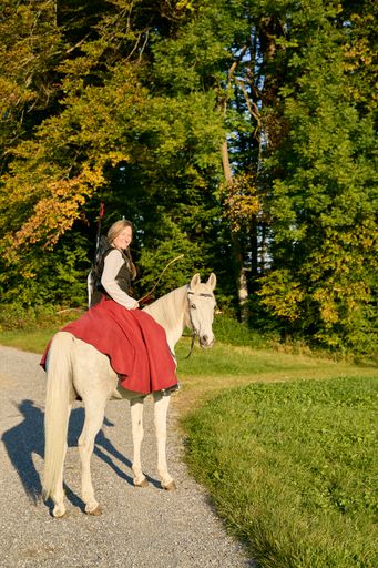 A vertical shot of a Caucasian female on a white horse with bow and arrows