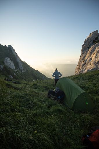 A tranquil scenery of a hiker outside the tent admiring the sunrise on top of the mountain