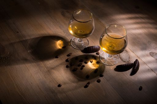 A high-angle shot of two glasses of brandy and coffee beans scattered on a wooden table