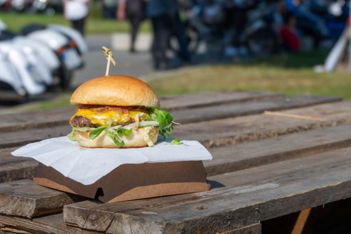 Cheeseburger outdoors on a rough wooden table with motorcycles in the background.