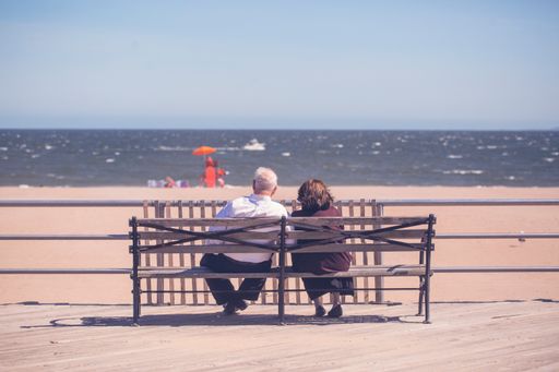 A scenic view of an old couple sitting on the bench in a sunny weather