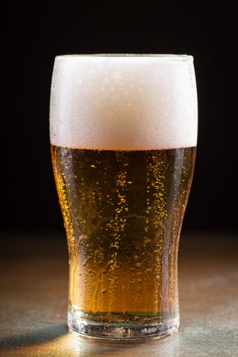A vertical shot of a glass of cold refreshing beer with foam on a wooden table