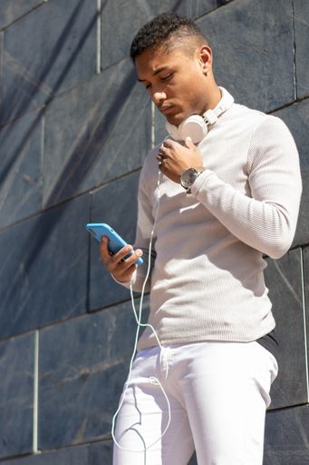 A vertical shot of a Hispanic guy holding his smartphone on the background of a stone wall.