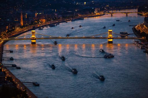 An aerial view of an illuminate bridge over the Danube river in Budapest with boats at night