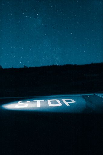 A vertical shot of an illuminated STOP sign on the road under a starry sky at night