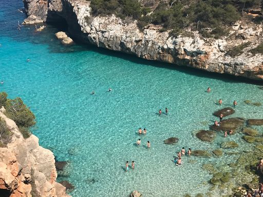 A high angle shot of people swimming in the turquoise sea water among rocky cliffs