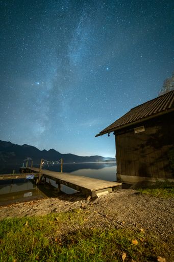 A scenic view of a starry night over a calm lake, wooden dock, and cabin