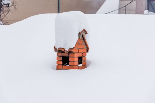 A closeup shot of a roof and chimney all covered with snow