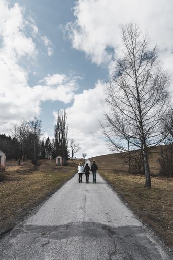 A vertical shot of three people walking on the road in an open field on a cloudy day-concept: family