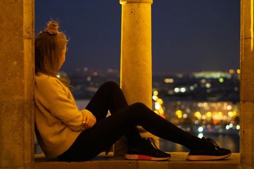 a beautiful view of a female sitting in an old place and  enjoying the beauty of Budapest at night